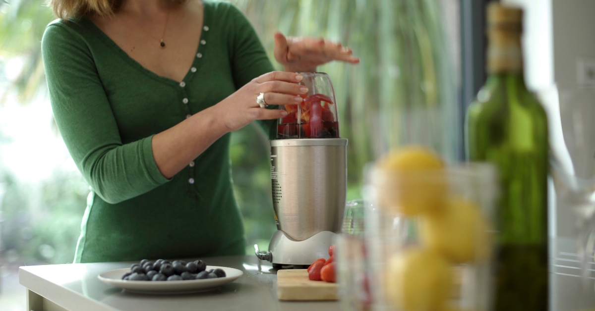 Lady loads up quiet smoothie maker on kitchen countertop.