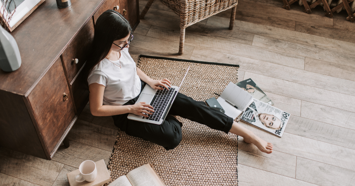 A woman sits on an apartment floor working on her laptop